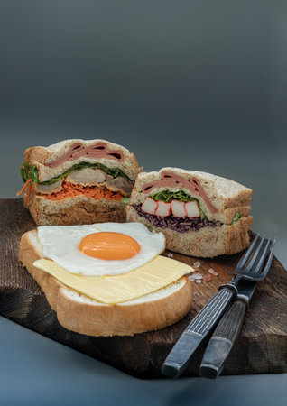 Homemade Sandwichs stuffed Ham, Cheese, Crab stick and vegetables with Cheese and Fried egg on  Bread served with knife and fork on wooden background. The concept of Healthy delicious food, Space for text, Selective Focus.の写真素材
