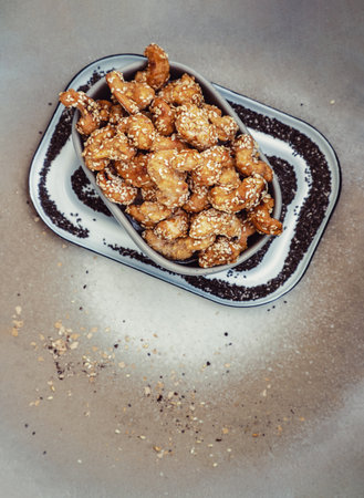 The view from above of Sweet Cashew Nuts coated with white sesame seeds in the ceramic bowl, put on the ceramic plate. Healthy snack, Space for text, Selective Focus.の写真素材