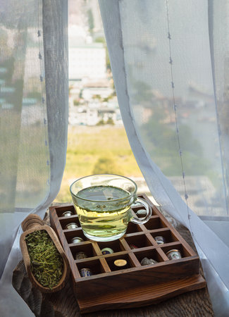 Refreshing and Enjoy with A cup of hot hemp tea (CBD herbal tea) and Dried organic hemp leaves on Vintage thimbles collection placed on an Old wooden box on old rustic wooden table by the window view with sunlight. Healthy drink concept. Space for text.の写真素材