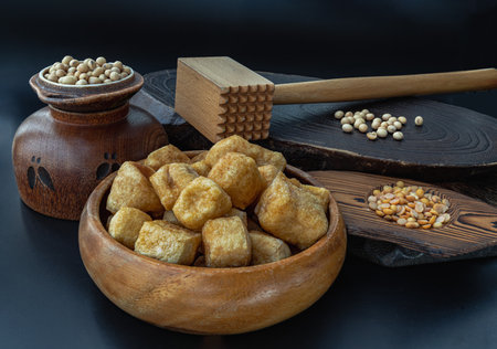 Brown fried tofu puffs or Deep Fried Tofu in wooden bowl and grains (soybeans) with dark background. Space for text.の写真素材