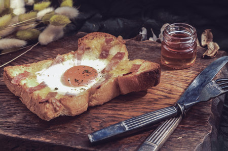 Homemade fried egg in a hole Bacon and Cheese toast serve with Honey on wooden cutting board. Sandwiches for breakfast, The concept of delicious food, Selective Focus.の写真素材