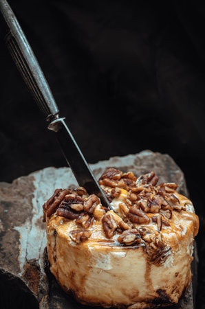 The black metal knife is inserted into the Caramel Pecan topped with caramel frosting and pecans on rock with dark background. Copy space, Selective focus.の写真素材