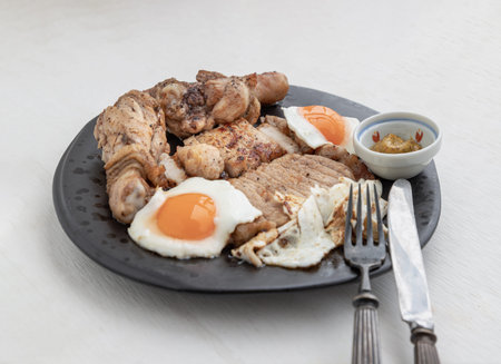 Sliced ââpork steak, Fried chicken drumsticks and Fried eggs for dinner are served with dipping sauce on ceramic plate. A plate of favorite food, Space for text, Selective Focus.の写真素材