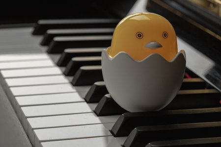 Baby chickÂ cartoon sitting in broken egg stand on the Piano Keyboard. Yellow cute chicken...