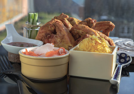Homemade yellow jasmine rice (Chicken biryani) served with Fried chicken wings, Pickled carrot and Radish, Cucumber sticks and sweet chili sauce on black table. Halal food, Space for text, Selective focus.の写真素材