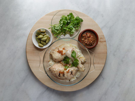 Delicious Steam chicken with rice (Hainanese chicken rice) serve with Pickled garlic, Cucumber and Chili sweet sauce on round wooden tray. Halal food, Top view, Space for text, Selective focus.の写真素材