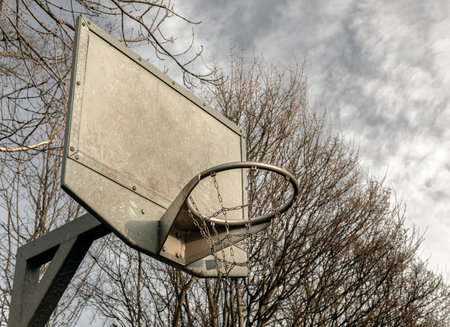 Edinburgh, Scotland, Jan 19, 2024 - Side view of Steel basketball backboard with the hoop metal ring and steel chain net against branches and sky. Street basketball court, Space for text, Selective focus.の写真素材