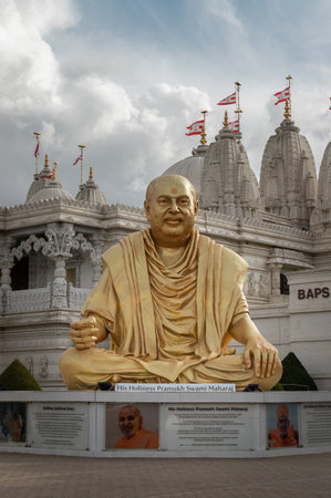 London, UK - Feb 23, 2024 - The gold colored statue of spiritual leader holiness pramukh swami maharaj front of Neasden temple (BAPS Shri Swaminarayan Mandir) against a nice cloudy sky background.のeditorial素材