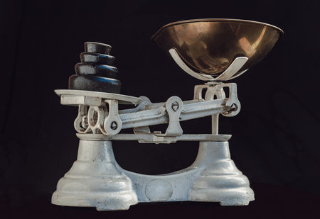 Classic weight scale Isolated on dark background. Old obsolete manual weighing scales and Iron Brass Tray with set of cast iron weights. Antique balance scales, Space for text, Selective Focus.の写真素材
