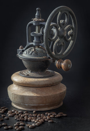 Antique coffee bean original grinder metal shake wheel with hand crank and coffee beans on dark background. Old original coffee grinder with traces of time and scuffs on the body, Space for text, Selective focus.の写真素材