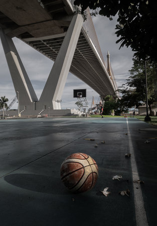 Basketball ball on the Old cement court floor at Outdoor park with Suspension bridge and Sky in the background. Space for text, Selective focus.のeditorial素材