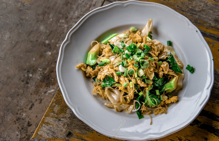 Stir-fried Noodles in Sweet Soy Sauce with Pork ( Pad See-Ew ) served in white dish on wooden table, Thai Style food, Top view, Selective focus.の写真素材