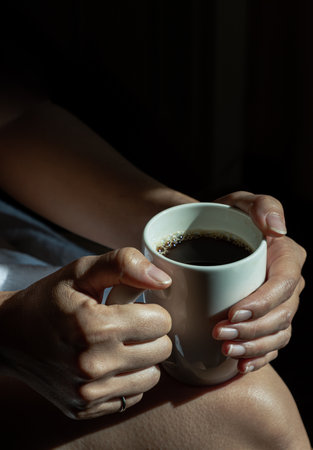 Close-up of Comforting cozy female hands holding a coffee mug with the morning sunlight that shines through. Dark tone, use it as your Wallpaper, Poster and Copy space, Selective focus.の写真素材
