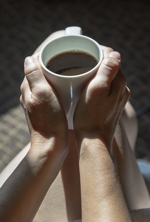 Comforting cozy female hands holding a coffee mug with the morning sunlight that shines through. Morning happy time, use it as your Wallpaper, Poster and Space for text, Selective focus.の写真素材