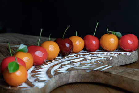 View of Traditional thai sweet treats made from mung beans and coconut milk, and glazed in shiny agar agar jelly. Imitation fruits (Kanom look choup) in the shape of fruits has a sweet taste on wooden cutting board. Thai dessert, use it as your Wallpaper, Poster and Copy space, Selective focus.の写真素材