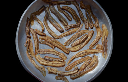 Top view of Natural Dehydrated Bananas on steel round tray with Black background. Delicious sun-dried Sliced Banana, Top view, use it as your Wallpaper, Poster and Space for text, Selective focus.の写真素材