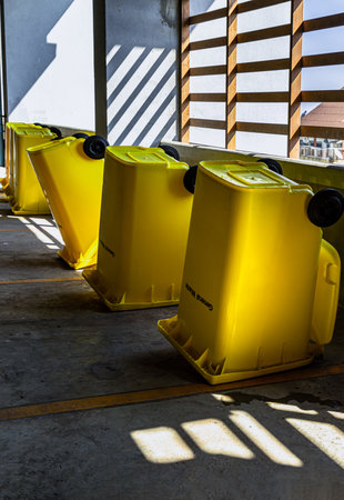 Bangkok, Thailand - Jan 18, 2025 - Perspective view of Yellow large plastic rubbish bins and turn upside down to dry near concrete wall on parking lot of condominium building. After cleaning big plastic yellow garbages container, Plastic trash with lid for general waste, selective focus.の写真素材