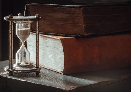 View of hourglass (Sandglass) with Ancient books on dark background. Light and Shadow, use it as your Space for text, Design, and Poster, Selective focus.の写真素材