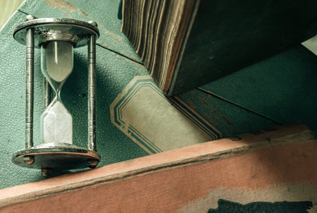 View of Silver hourglass or Sandglass with Old books on Vintage wooden box. The value of time, Light...