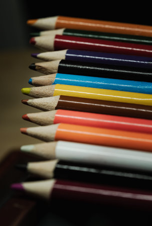 Perspective view of Multi colored pencils or wooden crayons to each other arranged in a neat row on dark background. The arrangement of the colors pencils creates a sense of unity. Pencils made of natural eco-friendly materials safe for children, Stationery for drawing and creativity, Empty space for text, design and wallpaper, Selective focus.の写真素材