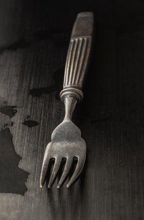 View of Black worn metal vintage fork in dark tone. Ancient vintage fork isolated on black background, Highlighting its texture and design, use it as your Space for text, Design, Wallpaper and Poster, Selective focus.の写真素材