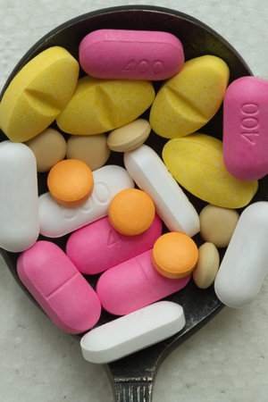 Top down view close up of A lot of pills of different colors and shapes stacked together on metal spoon with white background. Concept of medication treatment and Health care, use it as your Space for text, Design, Wallpaper and Poster, Selective focus.の写真素材