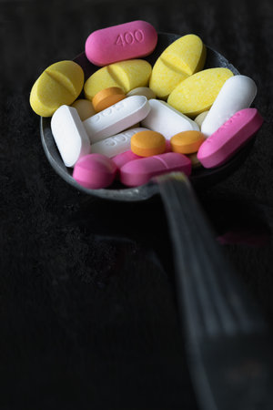 Perspective view of A lot of pills of different colors and shapes on Ancient vintage spoon isolated on black background. Concept of medication treatment and Health care, use it as your Space for text, Design, Wallpaper and Poster, Selective focus.の写真素材
