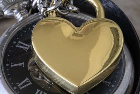 Close-up of Golden heart shaped love padlock on A retro pocket watch. Love can endure beyond the...