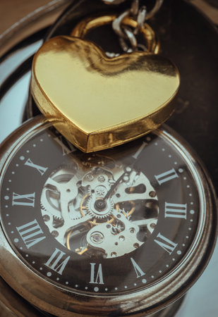 Close-up of Golden heart shaped love padlock lap over A retro pocket watch. Love can endure beyond the limitations of time, Concept of Love that transcends time, Valentine's day, use it as your Copy space, Design, Wallpaper and Poster, Selective focus.の写真素材
