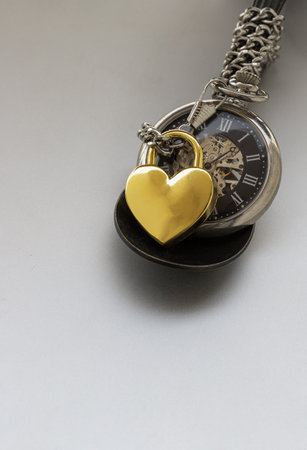 Golden heart shaped love padlock lap over A retro pocket watch on white background. Love can endure beyond the limitations of time, Concept of Love that transcends time, Valentine's day, use it as your Copy space, Design, Wallpaper and Poster, Selective focus.の写真素材