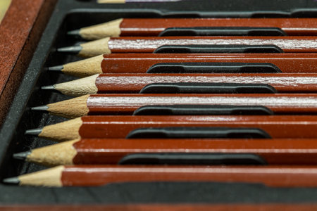 Perspective view of Wooden pencils arranged in a neat row in wooden pencil case on dark background. The arrangement of the colored pencils creates a sense of unity. Pencils made of natural eco-friendly materials safe for children, Empty space for text, design and wallpaper, Selective focus.の写真素材