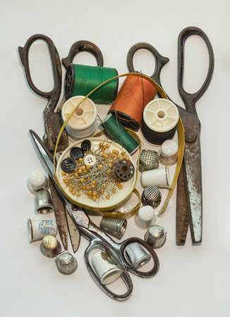 Steel scissors, Thimbles in small wooden treasure chest, Spools of thread of various colour, Sewing needles stuck in a green miniature spools thread and Measuring tape including Pins and Buttons in small round tray on White background. Sewing items set or Sewing notions (Sewing objects), Top view, use it as your Wallpaper, Poster and Copy space, Selective focus.の写真素材
