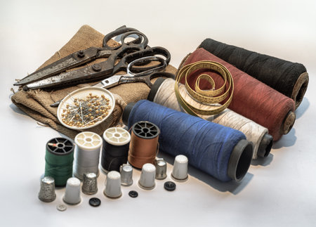 Steel scissors and Pins in small round tray on Sackcloth with Measuring tape on Spools of thread of various colour and Thimbles, Black buttons on white background. Sewing items set or Sewing notions (Sewing objects), use it as your Wallpaper, Poster and Space for text, Selective focus.の写真素材