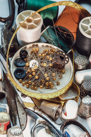 Sewing needles stuck in a green miniature spools thread Steel scissors, Spools of thread of various colour, Thimbles and Measuring tape including Pins and Buttons in small round tray. Sewing items set or Sewing objects (Sewing notions), use it as your Wallpaper, Poster and Copy space, Selective focus.の写真素材