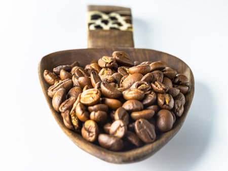 Perspective view of Roasted coffee beans on a rich textured surface in Wooden coffee scoop isolated on the white background. Enjoy your morning coffee for living, use it as your Space for text, Design, Wallpaper and Poster, Selective focus.の写真素材
