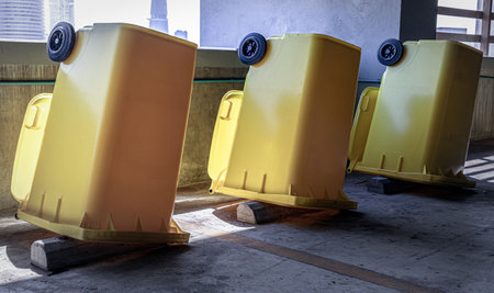 View of After cleaning big plastic yellow garbage container and turn upside down to dry. Yellow large plastic rubbish bin near concrete wall on parking lot of condominium building, Plastic trash with lid for general waste, selective focus.の写真素材