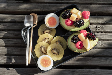 Top view of vibrant healthy food with blackberry, redberry and mango on avocado with golden kiwi and...