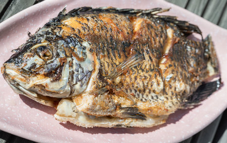 Delicious Deep Fried Whole Tilapia Fish on Ceramic fish plate on wooden background. use it as your...
