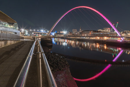 Newcastle, UK - Apr 13, 2025 - Nightscape view of The Iconic gateshead millennium bridge with Tyne bridge and dark sky in the background. The pedestrian bridge spanning the River tyne with reflection in river, use it as your Wallpaper, Poster and Copy space, Selective focus.の写真素材