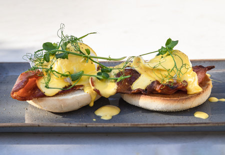 Eggs Benedict made with english muffin, grilled bacon, a brace of poached hen's eggs & hollandaise sauce and watercress served on ceramic tray. use it as your Wallpaper, Poster and Space for text, Selective focus.の写真素材