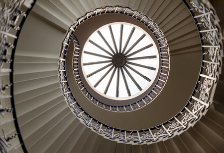 London, UK - Jun 18, 2025 - the iconic Tulip Stairs located in the Queen's House, a historic building in Greenwich, The handrail is adorned with decorative floral motifs, wrought iron structure was the first geometric self-supporting spiral staircase in Britain, a glorious view of the sweeping spiral stairs leading to the upper levels, use it as your Wallpaper, Poster and Space for text, Selective focus.の写真素材
