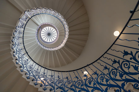 London, UK - Jun 18, 2025 - the iconic Tulip Stairs located in the Queen's House, a historic building in Greenwich, The handrail is adorned with decorative floral motifs, wrought iron structure was the first geometric self-supporting spiral staircase in Britain, a glorious view of the sweeping spiral stairs leading to the upper levels, use it as your Wallpaper, Poster and Space for text, Selective focus.の写真素材