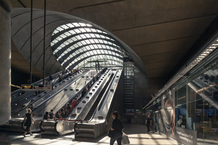 London, UK - Jun 18, 2025 - People and travelers utilizing the escalators within Canary Wharf tube station is a London in the Canary Wharf financial district of East London, The station is known for its distinctive architecture, which includes a large, curved glass roof that allows natural light into the concourse and long escalators leading down to the platforms. use it as your Wallpaper, Poster and Space for text, Selective focus.の写真素材