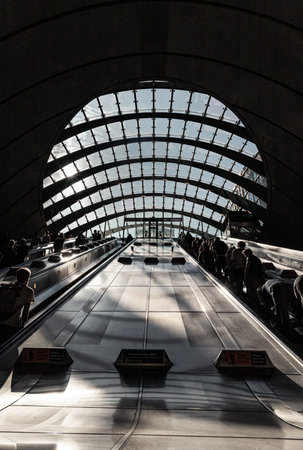 London, UK - Jun 18, 2025 - People and travelers utilizing the escalators within Canary Wharf tube station is a London in the Canary Wharf financial district of East London, The station is known for its distinctive architecture, which includes a large, curved glass roof that allows natural light into the concourse and long escalators leading down to the platforms. use it as your Wallpaper, Poster and Space for text, Selective focus.の写真素材