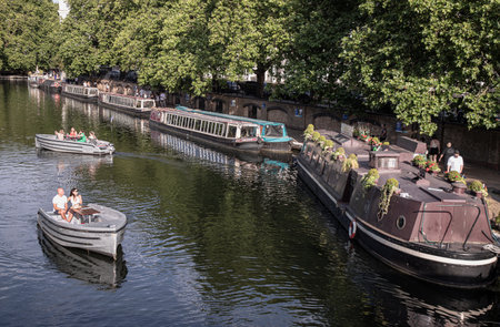 London, UK - Jun 21, 2025 - Tourist are relaxing on a Waterdream boat in Little Venice in West London at evening, It is the junction point of the Grand Union Canal and the Regent's, its tranquil canals and waterways lined with narrowboats and houseboats. use it as your Wallpaper, Poster and Copy space, Selective focus.の写真素材
