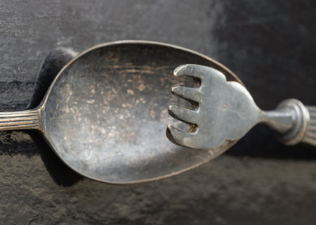 Close-up of Ancient worn vintage cutlery on the dark background. Crossed black metal spoon and fork in dark tone, Highlighting its texture and design, use it as your Space for text, Design, Wallpaper and Poster, Selective focus.の写真素材