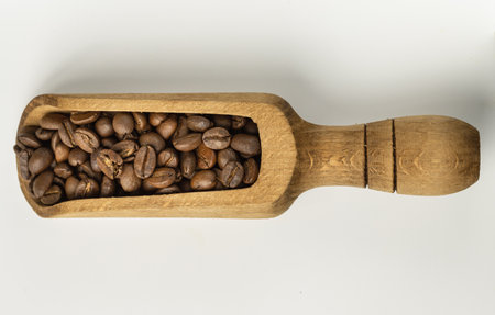 View of Roasted coffee beans on a rich textured surface in Wooden coffee scoop isolated on White background. Enjoy your morning coffee for living, use it as your Space for text, Design, Wallpaper and Poster, Selective focus.の写真素材