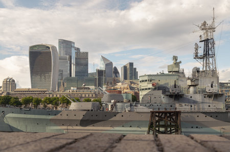 London, UK - Jul 21, 2025 - View of HMS Belfast (a historic warship) positioned prominently in the foreground, with the distinctive skyscrapers of London's financial district in the background. creating a contrast between historical and modern elements of the city, use it as your Wallpaper, Poster and Copy space, Selective focus.の写真素材