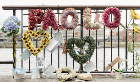 London, UK - Jul 21, 2025 - The floral tributes on the iron railing, including the name "MALO" spelled out in flowers, are indeed part of a memorial for victims of the London Bridge terror attack in 2017. These tributes are placed at or near the site of the tragic event as a way to commemorate those who lost their lives and to express grief and remembrance. use it as your Wallpaper, Poster and Copy space, Selective focus.の写真素材