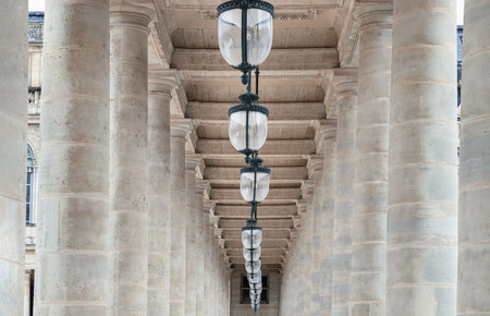 France, Paris - May 03, 2025 - Corridor perspective with Columns and Antique lantern hanging from Ceiling inside of the Courtyard of the Honor gallery in the National estate of the Palais-Royal. use it as your Wallpaper, Poster and Copy space, Selective focus.の写真素材